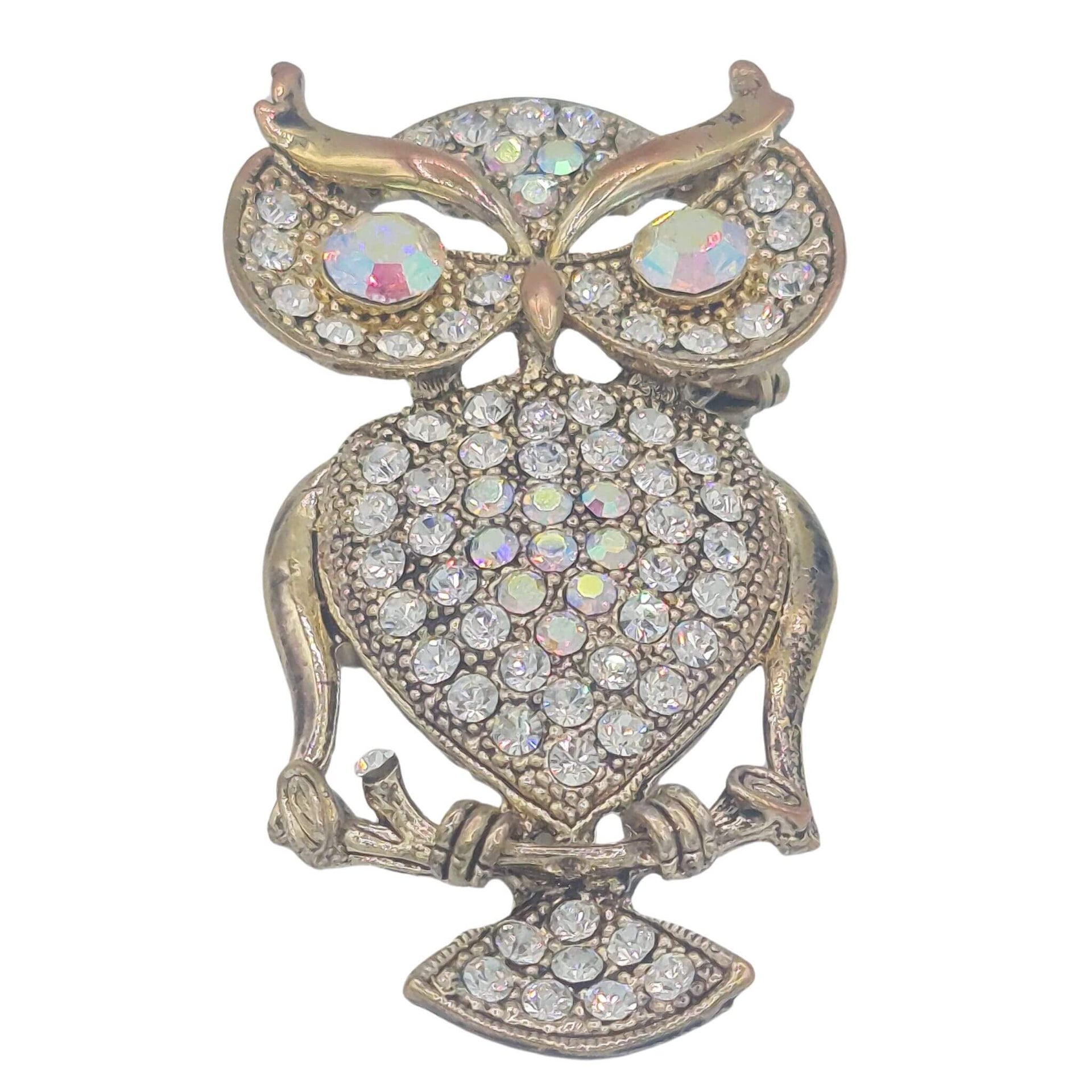 Broche buho colgante de metal dorado y brillantes de strass en color blanco. Trasera en color oro viejo con alfiler y seguro. Puede usarse también como colgante con una cadena ya que lleva una argolla en la parte superior. Mide 6 cm de largo x 3 cm de ancho.