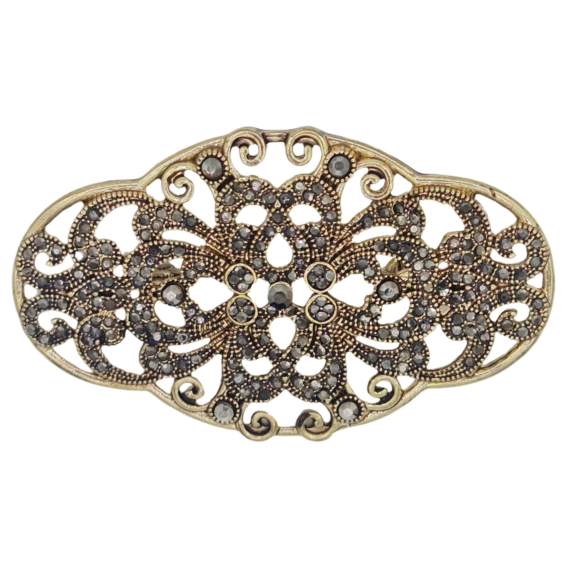 Broche metal dorado y brillantes de strass en gris oscuro. Mide 8 cm de largo por 4 cm de alto. El alfiler trasero es de 6 cm con cierre de seguridad.