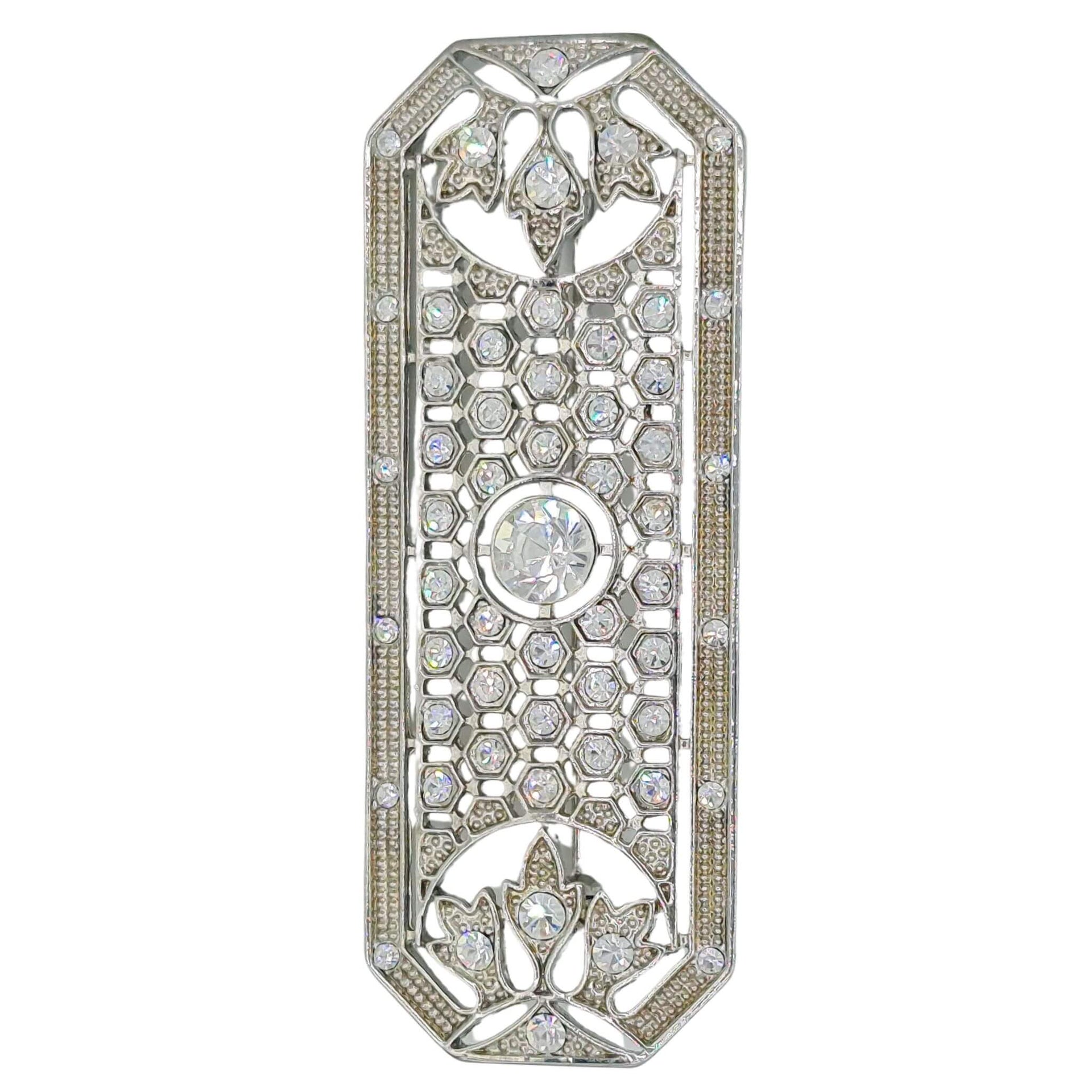 Broche rectangular en metal plateado y brillantes de strass en color blanco. Mide 8 cm de largo por 3 cm de ancho. El alfiler trasero es de 6 cm con cierre de seguridad. Un complemento ideal para lucir como broche sobre la ropa, un bolso, un sombrero o un collar.