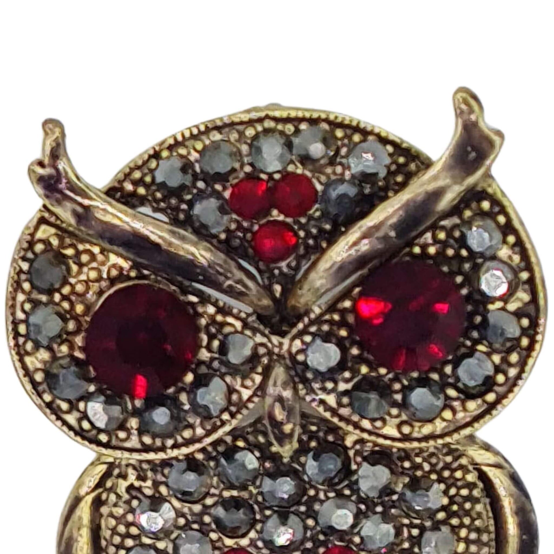 Broche colgante  buho de metal dorado y brillantes de strass en color rojo. Trasera en color oro viejo con alfiler y seguro. Además del alfiler habitual, lleva una pieza que permite usarlo como colgante. Mide 6 cm de largo x 3 cm de ancho.