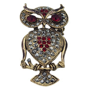 Broche colgante  buho de metal dorado y brillantes de strass en color rojo. Trasera en color oro viejo con alfiler y seguro. Además del alfiler habitual, lleva una pieza que permite usarlo como colgante. Mide 6 cm de largo x 3 cm de ancho.