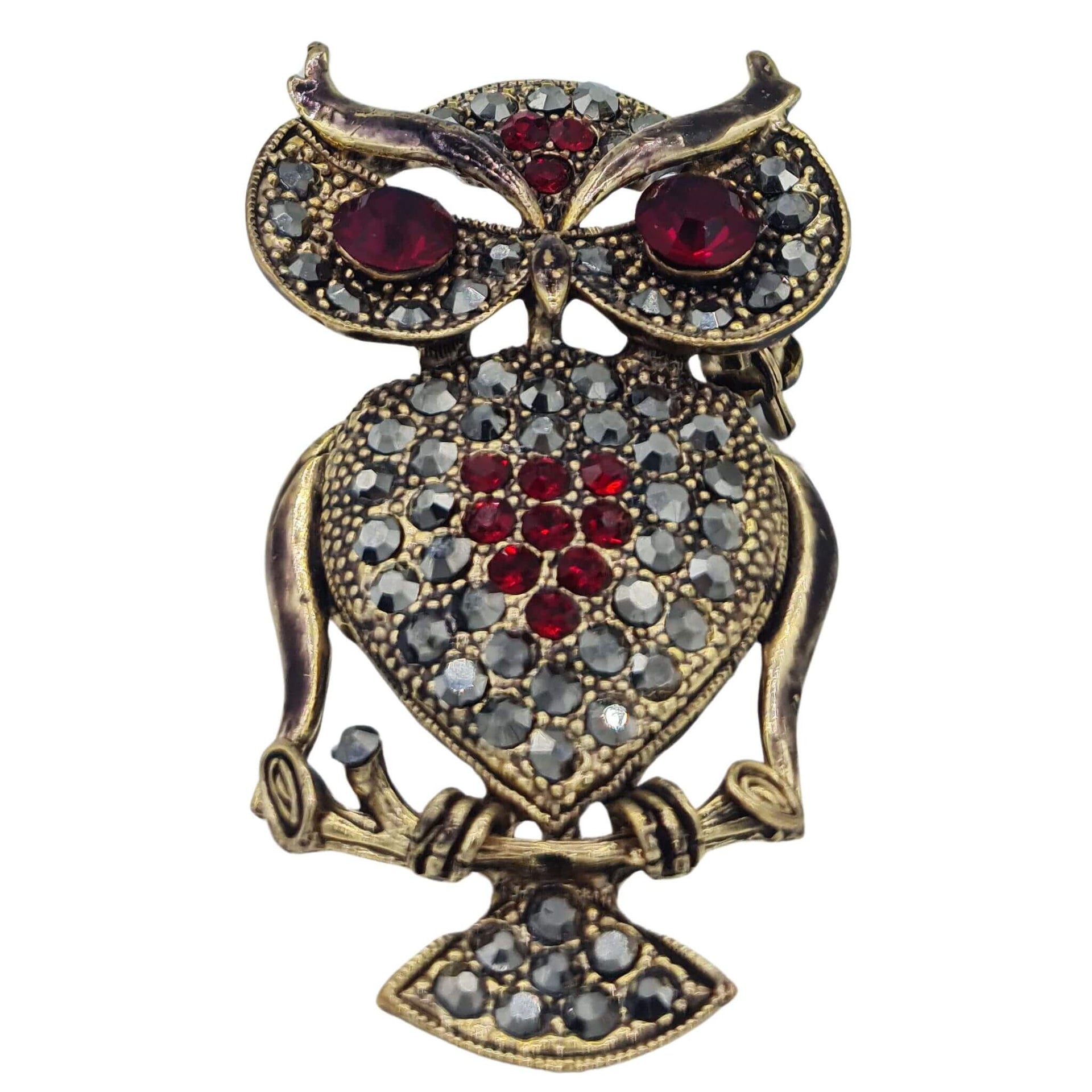 Broche colgante  buho de metal dorado y brillantes de strass en color rojo. Trasera en color oro viejo con alfiler y seguro. Además del alfiler habitual, lleva una pieza que permite usarlo como colgante. Mide 6 cm de largo x 3 cm de ancho.