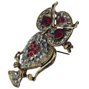 Broche colgante  buho de metal dorado y brillantes de strass en color rojo. Trasera en color oro viejo con alfiler y seguro. Además del alfiler habitual, lleva una pieza que permite usarlo como colgante. Mide 6 cm de largo x 3 cm de ancho.