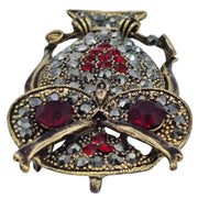 Broche colgante  buho de metal dorado y brillantes de strass en color rojo. Trasera en color oro viejo con alfiler y seguro. Además del alfiler habitual, lleva una pieza que permite usarlo como colgante. Mide 6 cm de largo x 3 cm de ancho.