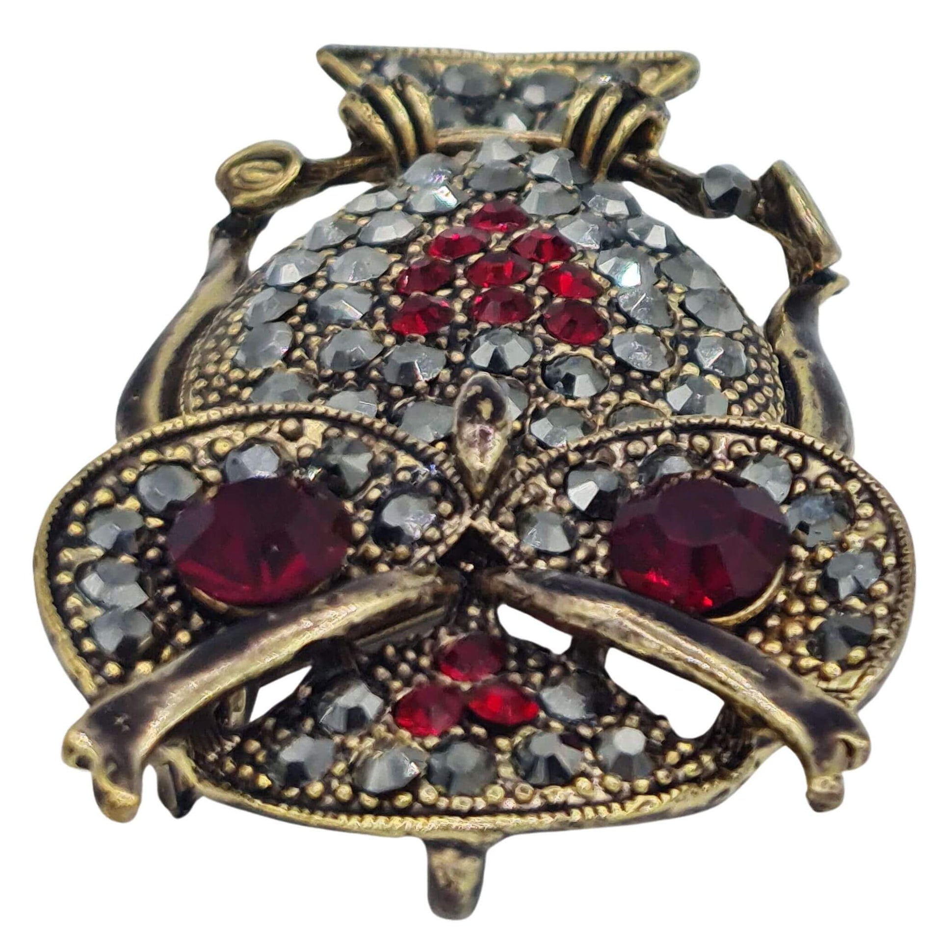 Broche colgante  buho de metal dorado y brillantes de strass en color rojo. Trasera en color oro viejo con alfiler y seguro. Además del alfiler habitual, lleva una pieza que permite usarlo como colgante. Mide 6 cm de largo x 3 cm de ancho.